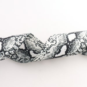May include: A white and black ribbon with a snakeskin pattern. The ribbon is curled and twisted.