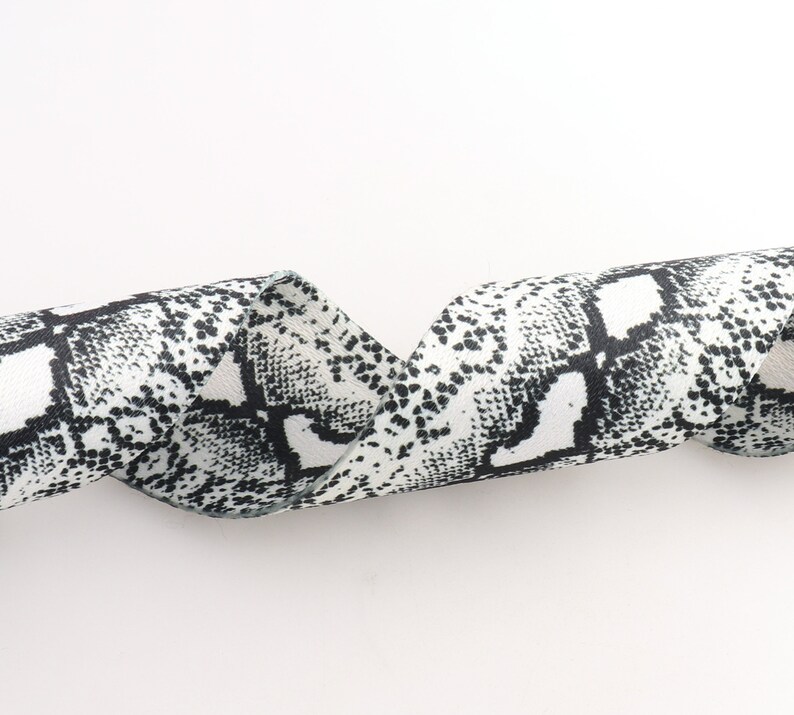 May include: A white and black ribbon with a snakeskin pattern. The ribbon is curled and twisted.