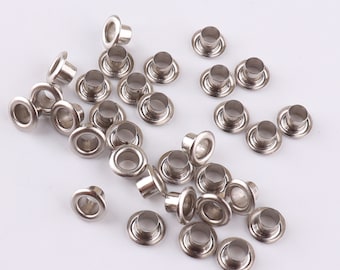May include: A large group of silver metal eyelets, commonly used for crafts and clothing alterations.