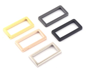 Puede incluir: Cinco anillos rectangulares de metal en diferentes acabados: oro, oro rosa, plata, negro y gris oscuro. Estos anillos son ideales para sujetar a correas, bolsos u otros accesorios.