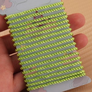 Può includere: Un rotolo di cordoncino verde lime, avvolto attorno a un supporto di cartone con un design a cartone animato. Il cordoncino è spesso circa 6 mm.