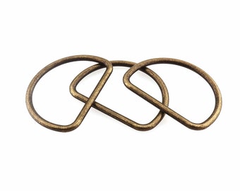 May include: Three antique gold-toned metal D-rings, interlocked together. The rings are smooth and have a slightly worn finish.