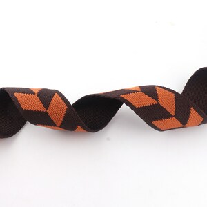 May include: Brown and orange striped webbing ribbon. The ribbon is woven with a geometric pattern.