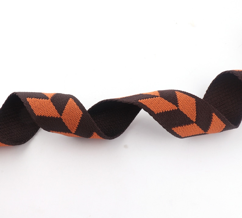 May include: Brown and orange striped webbing ribbon. The ribbon is woven with a geometric pattern.