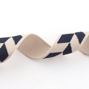 May include: Beige and navy blue woven ribbon with a geometric pattern. The ribbon is twisted and curled.