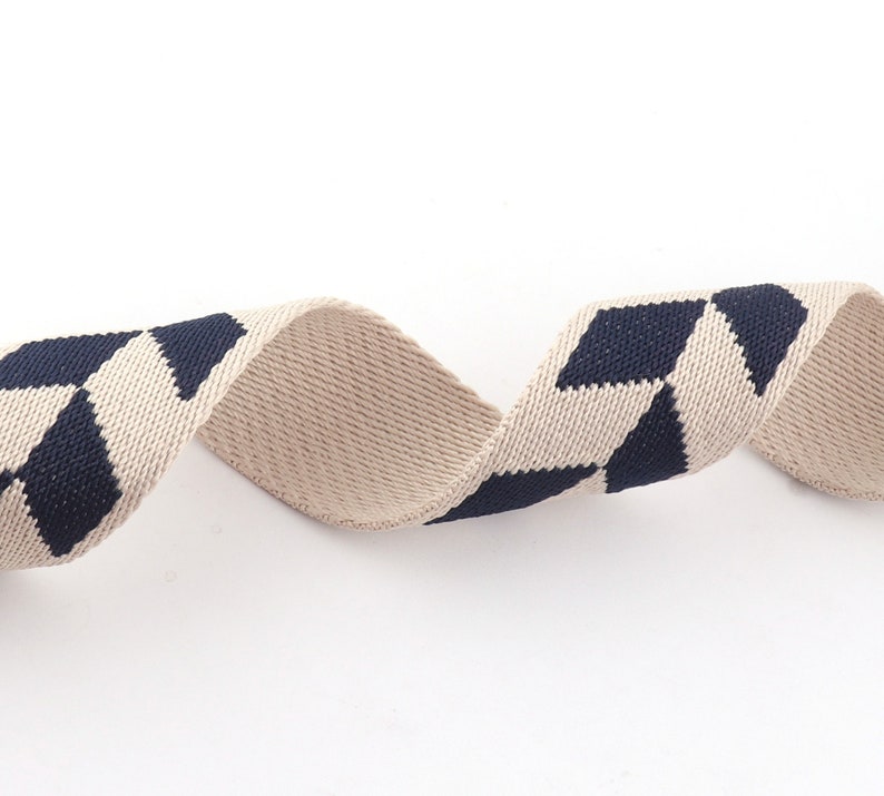 May include: Beige and navy blue woven ribbon with a geometric pattern. The ribbon is twisted and curled.