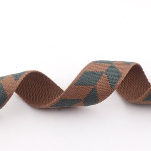 May include: Brown and green woven ribbon with a geometric pattern. The ribbon is twisted and curled.