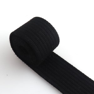 K&ouml;nnte beinhalten: Ein schwarzes Baumwollband, aufgerollt und auf einer wei&szlig;en Oberfl&auml;che liegend.