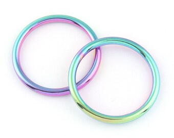 May include: Two iridescent metal rings with a rainbow finish. The rings are round and have a smooth, reflective surface. The colors shift from purple to green and blue. The rings are overlapping on a white background.