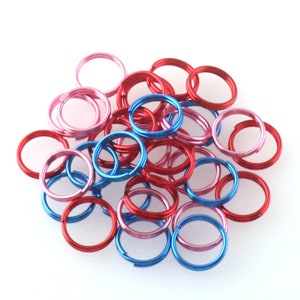 May include: A pile of small, colorful metal jump rings in red, blue, and pink. The rings are used for jewelry making and crafting.