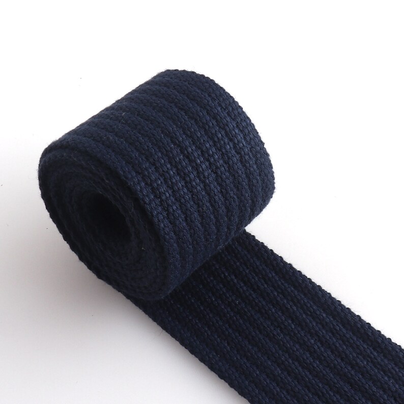 K&ouml;nnte beinhalten: Eine Rolle dunkelblaues Baumwollband, eine Art strapazierf&auml;higes Stoffband, das f&uuml;r Riemen, G&uuml;rtel und andere Anwendungen verwendet wird.