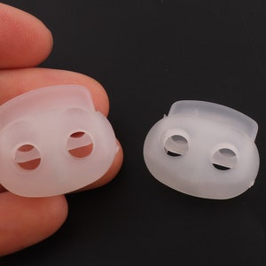 Puede incluir: Dos cierres de palanca de plástico blanco con dos agujeros cada uno. Los cierres son de forma ovalada y tienen una superficie lisa.