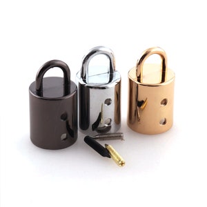 Peut inclure: Trois fermetures de sac en métal de forme cylindrique avec une boucle sur le dessus. Les fermetures sont en noir, argent et or.