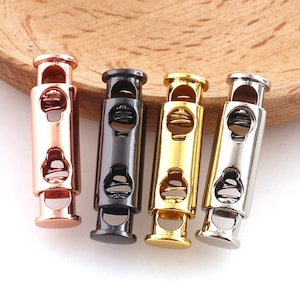 Op de afbeelding: Vier metalen koorduiteinden in verschillende afwerkingen: rosé goud, zwart, goud en zilver. Elk uiteinde heeft een veermechanisme en een lus om een koord aan te bevestigen.