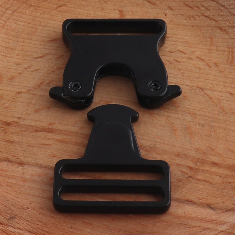 May include: Black plastic buckle with two parts. The top part has a D-ring shape and the bottom part has two slots.