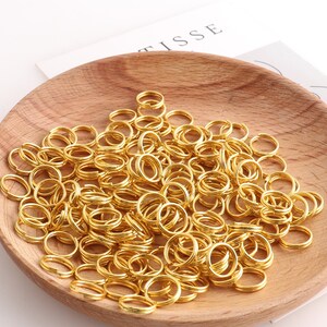 May include: A bowl filled with a large quantity of gold-colored metal jump rings. The rings are all the same size and are arranged in a random pattern.