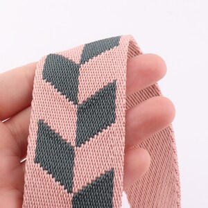 May include: Close-up of a pink and gray woven elastic band with a geometric pattern.
