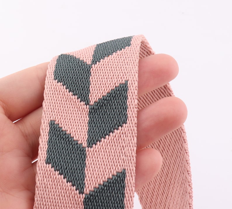 May include: Close-up of a pink and gray woven elastic band with a geometric pattern.
