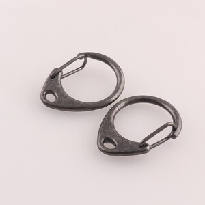 May include: Two black metal key rings with a swivel clasp. The key rings are oval shaped with a pointed end.