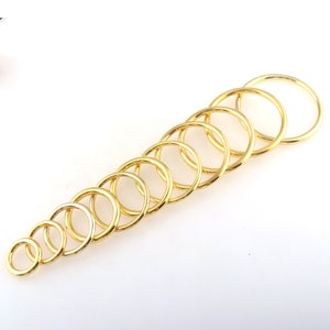May include: A set of ten gold-colored metal jump rings of varying sizes. The rings are arranged in a graduated size order, with the largest ring at the top and the smallest ring at the bottom.