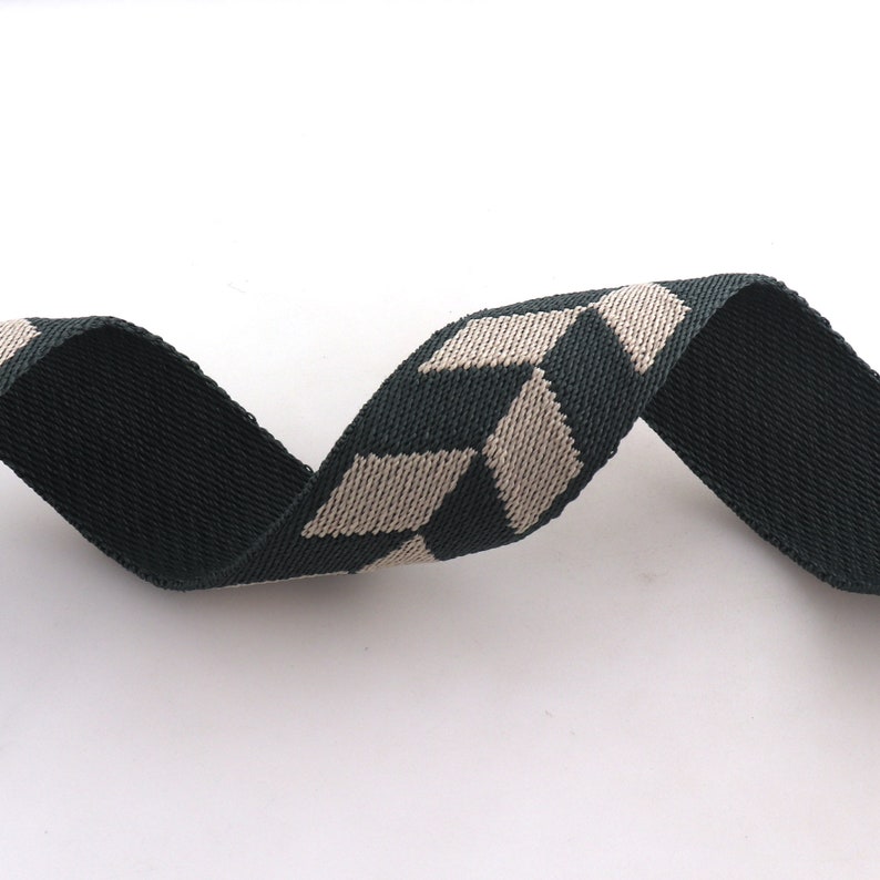 May include: A green and beige woven ribbon with a chevron pattern. The ribbon is soft and flexible, making it ideal for crafting projects.