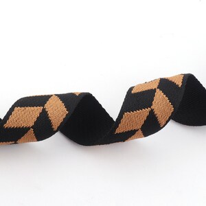 May include: Black and brown woven ribbon with a geometric pattern. The ribbon is curled and twisted.