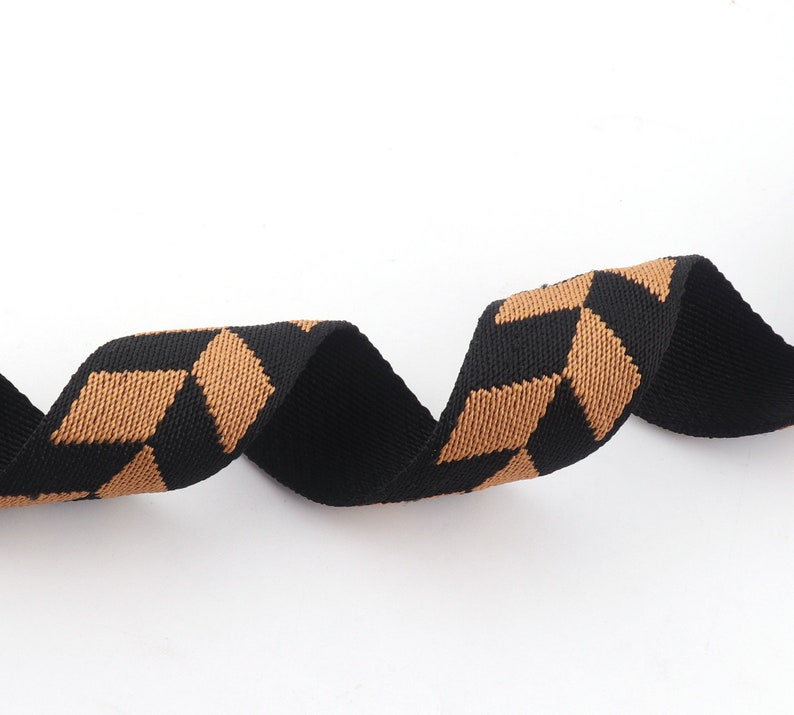May include: Black and brown woven ribbon with a geometric pattern. The ribbon is curled and twisted.