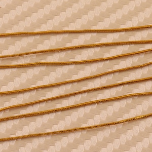 Puede incluir: Varias hebras de cordón metálico de color dorado, dispuestas en líneas paralelas sobre una superficie texturizada beige.