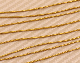 May include: Multiple strands of gold-colored elastic cord, arranged in parallel lines on a textured beige surface.