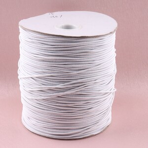 Puede incluir: Un carrete de cordón elástico blanco. El cordón está enrollado firmemente alrededor de un núcleo de cartón. El fondo es de color rosa liso. Este cordón se utiliza probablemente para proyectos de costura o artesanía.