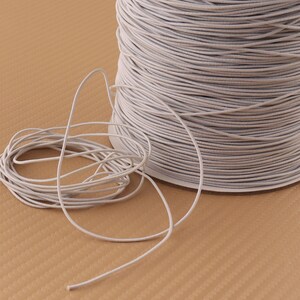 May include: A spool of white elastic cord. The cord is wound tightly around the spool and is ready to be used for crafting projects.