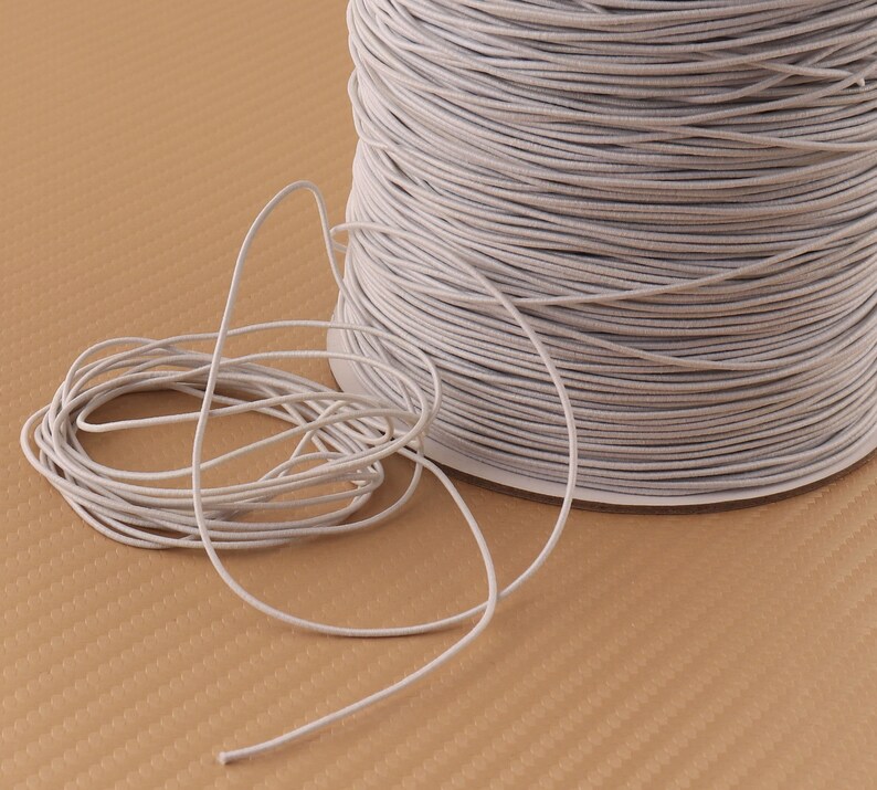 May include: A spool of white elastic cord. The cord is wound tightly around the spool and is ready to be used for crafting projects.