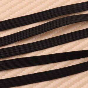 May include: Four black elastic bands, arranged in a diagonal pattern, on a beige textured surface.