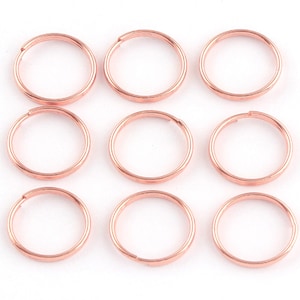 Pode incluir: Dez argolas de salto em ouro rosa, cada uma com uma forma circular lisa. Estas argolas são ideais para a fabricação de joias, artesanato e fixação de pingentes.