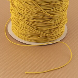 May include: A spool of bright yellow elastic cord. The cord is wound tightly around the spool and is ready to be used for crafting projects.