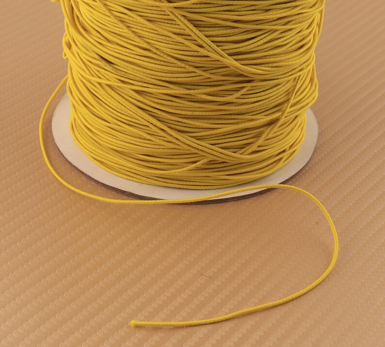 May include: A spool of bright yellow elastic cord. The cord is wound tightly around the spool and is ready to be used for crafting projects.
