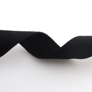 K&ouml;nnte beinhalten: Schwarzes Baumwollband, eine Art flaches, gewebtes Gewebe, ist in einer gekr&uuml;mmten Form dargestellt.