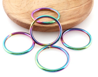 May include: Five iridescent metal rings, each with a different rainbow color pattern, are arranged on a white surface. The rings are all the same size and shape, and they are all made of a smooth, shiny metal.