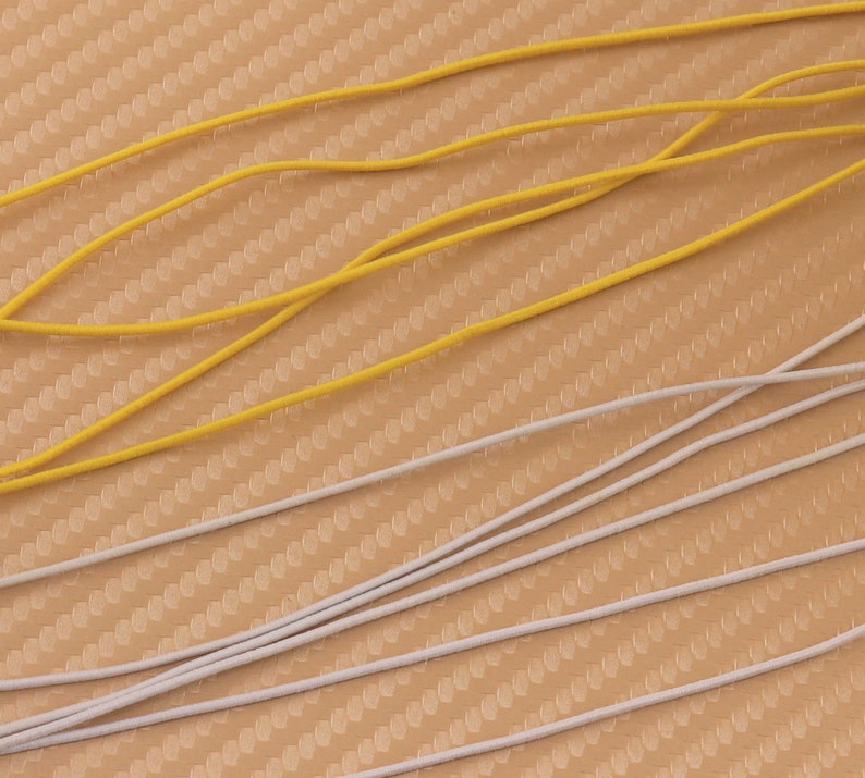 May include: A close-up of two types of elastic cord. One is yellow and the other is white. The cords are lying on a textured surface.
