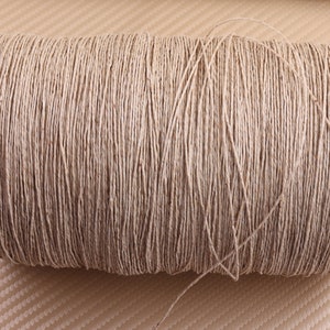 Puede incluir: Un carrete de cuerda de fibra natural, probablemente de yute o cáñamo, enrollado firmemente en un color beige. La cuerda es lisa y parece ser fuerte y duradera.