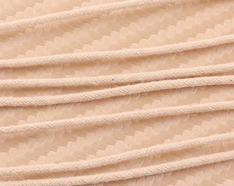 May include: Close-up of natural cotton cord, showing the texture and weave of the material. The cord is beige in color and is arranged in parallel lines.