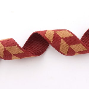 May include: Red and tan woven ribbon with a geometric pattern. The ribbon is curled and twisted.