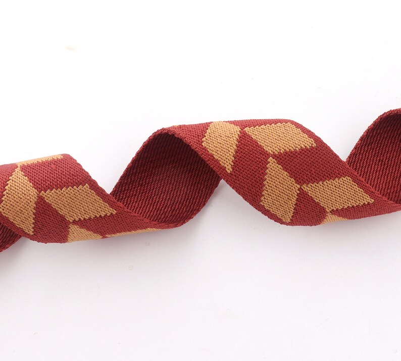 May include: Red and tan woven ribbon with a geometric pattern. The ribbon is curled and twisted.