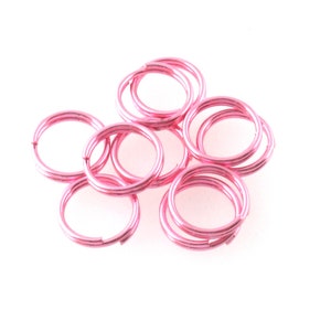 May include: A group of pink metal jump rings. The rings are small and round, and they are all linked together.