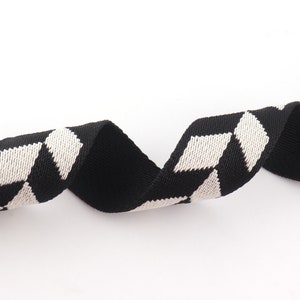 May include: Black and white woven ribbon with a geometric pattern. The ribbon is made of a soft, textured fabric.