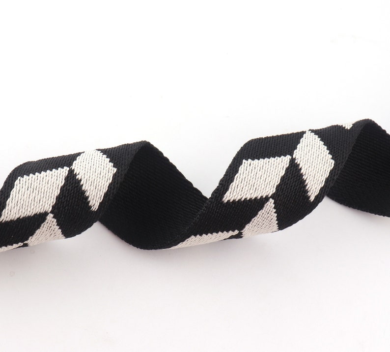 May include: Black and white woven ribbon with a geometric pattern. The ribbon is made of a soft, textured fabric.
