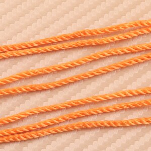 Può includere: Quattro fili di corda arancione sono disposti in linee parallele su uno sfondo color pesca testurizzato. La corda è intrecciata e ha una lucentezza sottile.
