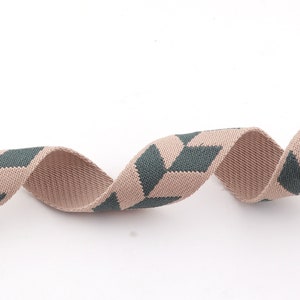 May include: A beige and dark green woven ribbon with a geometric pattern. The ribbon is curled and twisted.