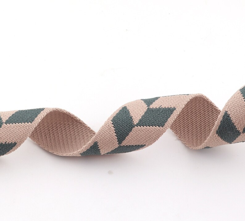 May include: A beige and dark green woven ribbon with a geometric pattern. The ribbon is curled and twisted.