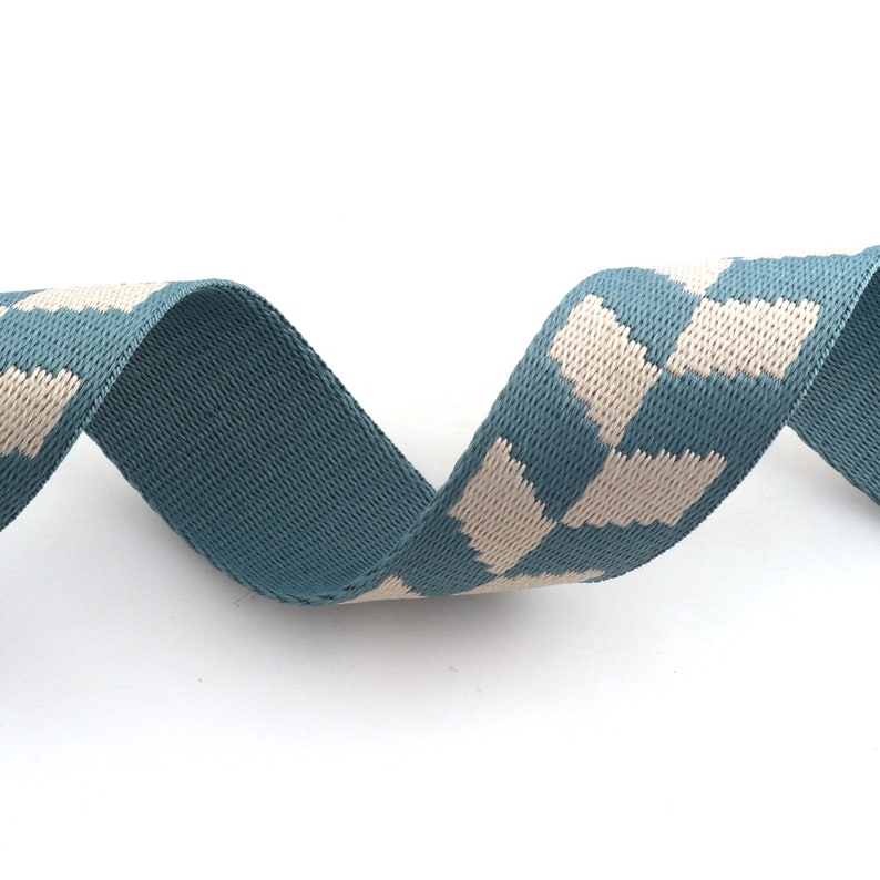 May include: A teal blue and white patterned ribbon with a geometric design. The ribbon is woven and has a soft texture.